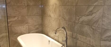 A bathroom with a freestanding bathtub, a glass shower enclosure, and a marble-tiled wall.