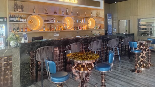 Zona de bar con un letrero 'MARIGOLD', mesas redondas y sillas azules.