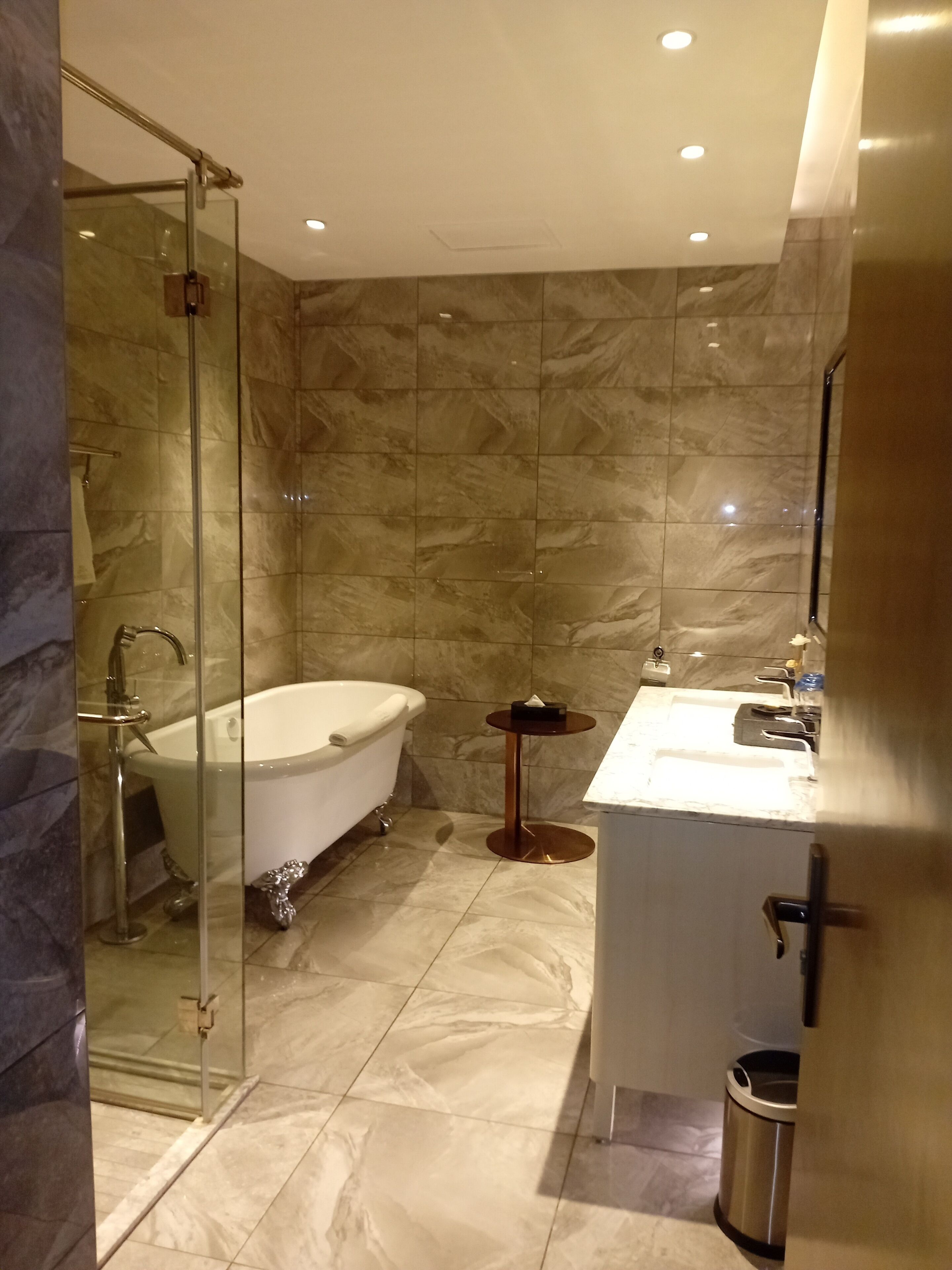 Un baño moderno con ducha de vidrio, una bañera independiente, un espejo redondo y un lavamanos blanco.
