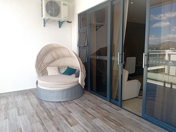 A balcony with a wicker chair, a glass door, and an air conditioning unit.