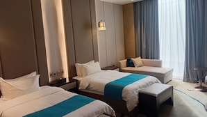 Habitación de hotel con dos camas, un sofá, una mesita y un ventanal con cortinas.