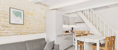 A modern kitchen with white cabinets, a wooden dining table, and a staircase.