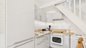 Une cuisine compacte avec des meubles blancs, un plan de travail en bois, un four Bosch et une machine à café.