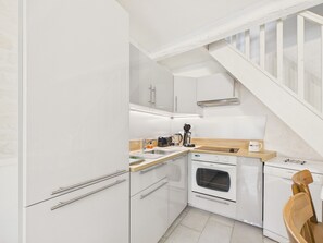 Eine kleine Küche mit weißen Schränken, einer Holz Arbeitsplatte, einem Bosch-Ofen und einer Kaffeemaschine.