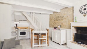Une cuisine avec un coin repas, un escalier, un mur en pierre et une cheminée.