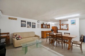 A living room with a sofa, a glass coffee table, a dining table with chairs, wooden cabinets, and wall-mounted decorations.