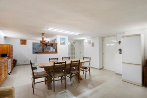A dining area with a wooden table and chairs, a white refrigerator, and a kitchen area with cabinets and a sink.