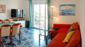 A living room with a red sofa, a television, a dining table with chairs, and a large window with curtains. - Casa Blu • Thermal Relax in the Center • Free Wi-Fi • 15 min. to the sea (Venturina Terme)