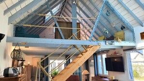 Ein Loft-Zimmer mit einer Holztreppe, einem Fernseher und einer gemütlichen Sitzecke.
