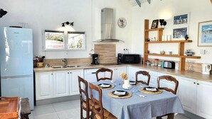 Eine Küche mit Esstisch, gedeckt für vier Personen, weißen Schränken, einer Mikrowelle, einer Kaffeemaschine und einer Uhr an der Wand.