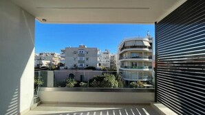 A balcony with a view of surrounding buildings, a closed shutter, and a clear sky. - Athenean Oasis In Ellinikon-Β2 (Elliniko)