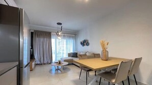 A modern living room with a dining table, chairs, a sofa, a coffee table, and a refrigerator. - Athenean Oasis In Ellinikon-Β2 (Elliniko)