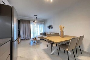 Ein modernes Wohnzimmer mit Esstisch, Stühlen, einer Couch, einem Couchtisch und einem Kühlschrank.