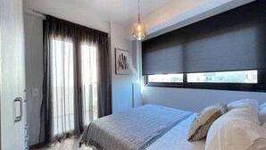 A bedroom with a bed, a window with blinds, a door, and a hanging light fixture. - Athenean Oasis In Ellinikon-Β2 (Elliniko)