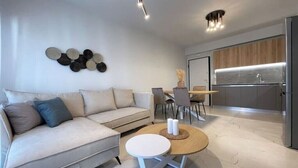 A modern living room with a sofa, a round coffee table, and a dining area with chairs. - Athenean Oasis In Ellinikon-Β2 (Elliniko)