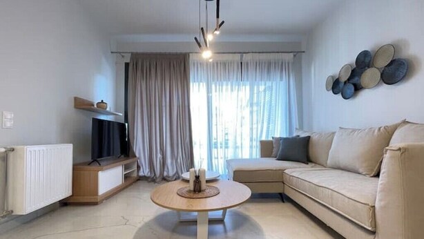 A modern living room with a round coffee table, a sofa, a TV on a stand, and a wall-mounted decoration. - Athenean Oasis In Ellinikon-Β2 (Elliniko)