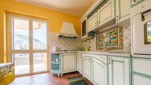 Een keuken met witte kasten, een betegelde spatwand en uitzicht door een schuifdeur.