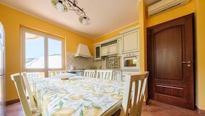 Een eetgedeelte met een tafel voor vier personen, een keuken met witte kasten en een grote houten deur.