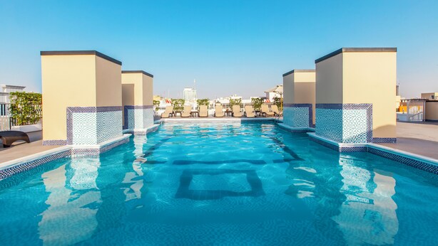 A swimming pool with tiled edges, lounge chairs, and a clear sky. - Golden Sands 5 Hotel Apartment (Dubai)