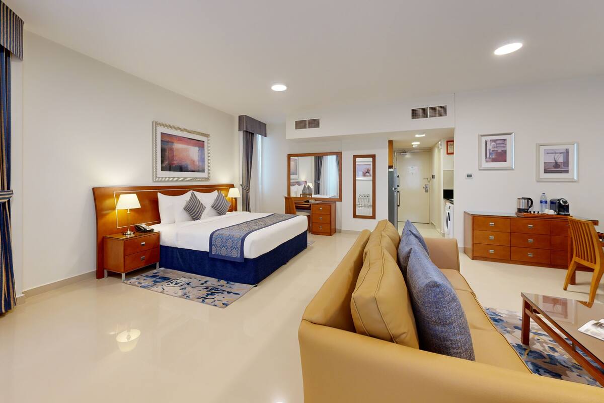Habitación de hotel con cama, sofá, escritorio, espejo y puerta que da a un baño.