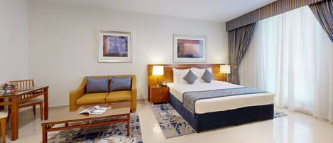 A hotel room with a bed, a sofa, a dining table, and two framed artworks on the wall.