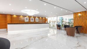 A modern reception area with a marble floor, wooden paneling, a chandelier, framed pictures, and seating. - Golden Sands 5 Hotel Apartment (Dubai)