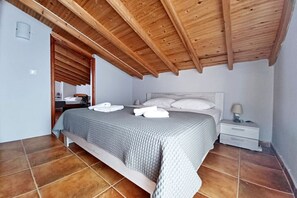 A bedroom with a wooden ceiling, a bed with white bedding, a nightstand, and a tiled floor. - Into The Breeze by RentalsPro - Kriopigi Halkidiki (Kriopighi)
