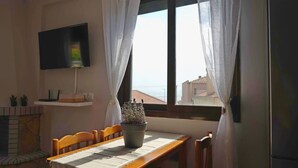 Ein Essbereich mit Tisch, Stühlen, einer Topfpflanze, einem Flachbildfernseher und einem Fenster mit Vorhängen.