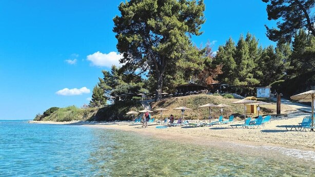 Ein Strand mit klarem Wasser, Sonnenschirmen und Liegestühlen.