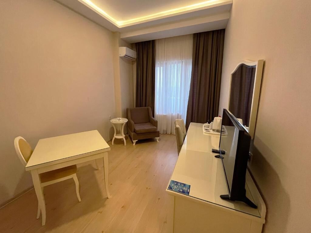 A hotel room with a desk, a chair, a television, a small table, and a window with curtains.