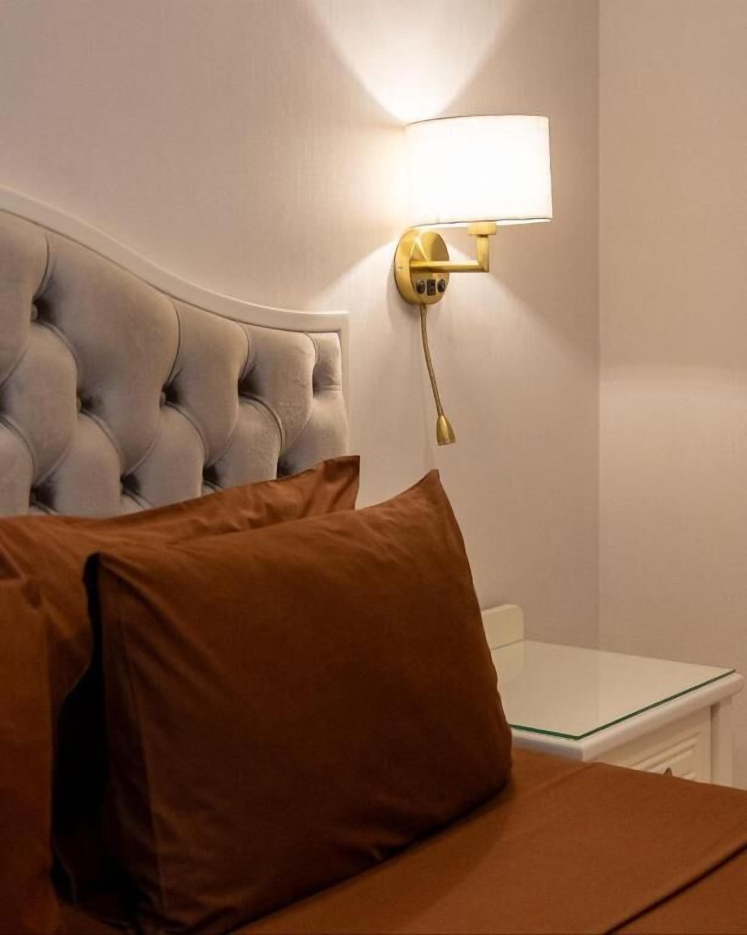 A bedroom with a tufted headboard, a bedside table, and a wall-mounted lamp.