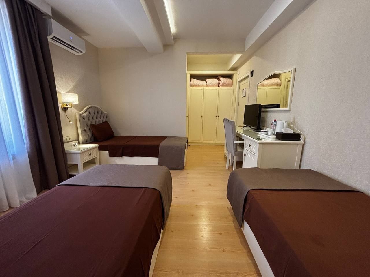 A hotel room with two single beds, a desk with a chair, a wardrobe, and a mirror on the wall.