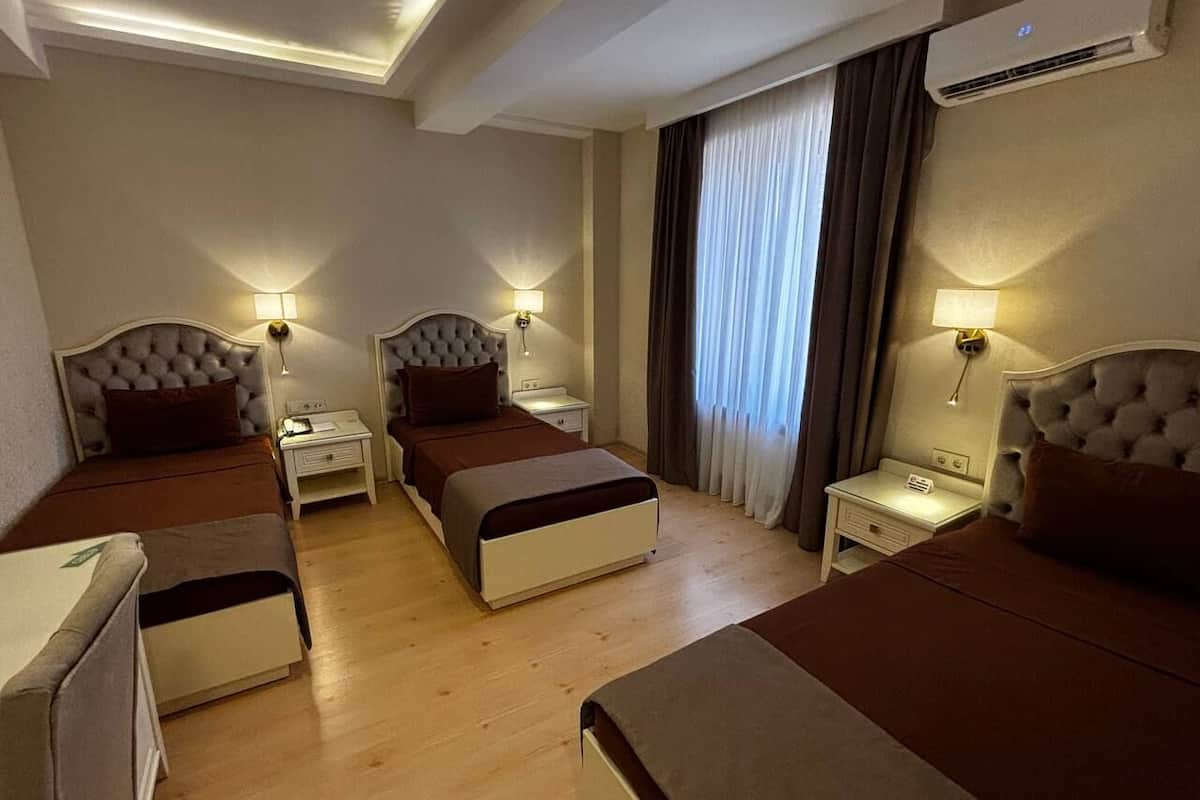 Quarto de hotel com duas camas, mesas de cabeceira, luminárias, ar condicionado e uma janela com cortinas.