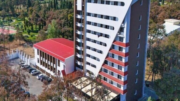 Un hotel de varios pisos con un diseño angular característico, techo rojo y un área de estacionamiento.