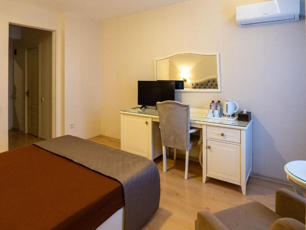 Hotelkamer met een bed, bureau met stoel, televisie, spiegel en een klein tafeltje met een kopje en fles.