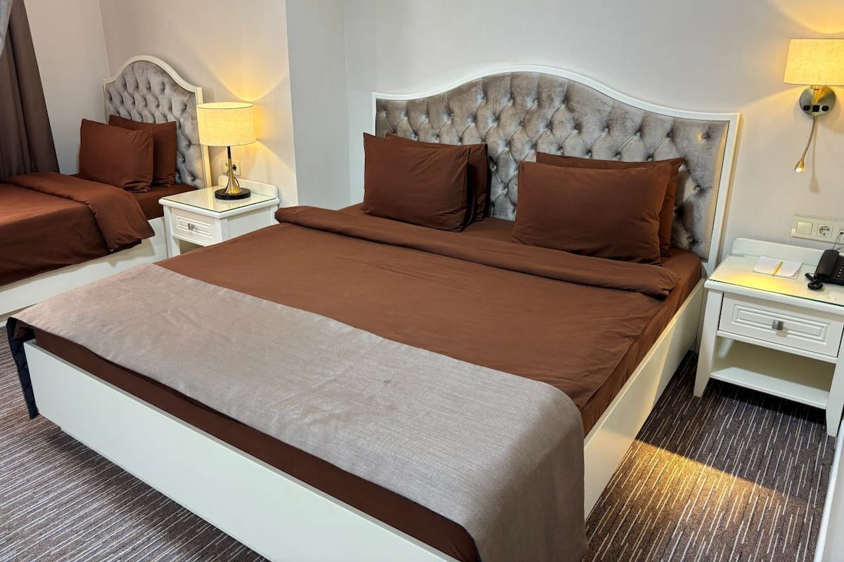 Quarto de hotel com uma cama grande, duas mesas de cabeceira, uma luminária e um criado-mudo.