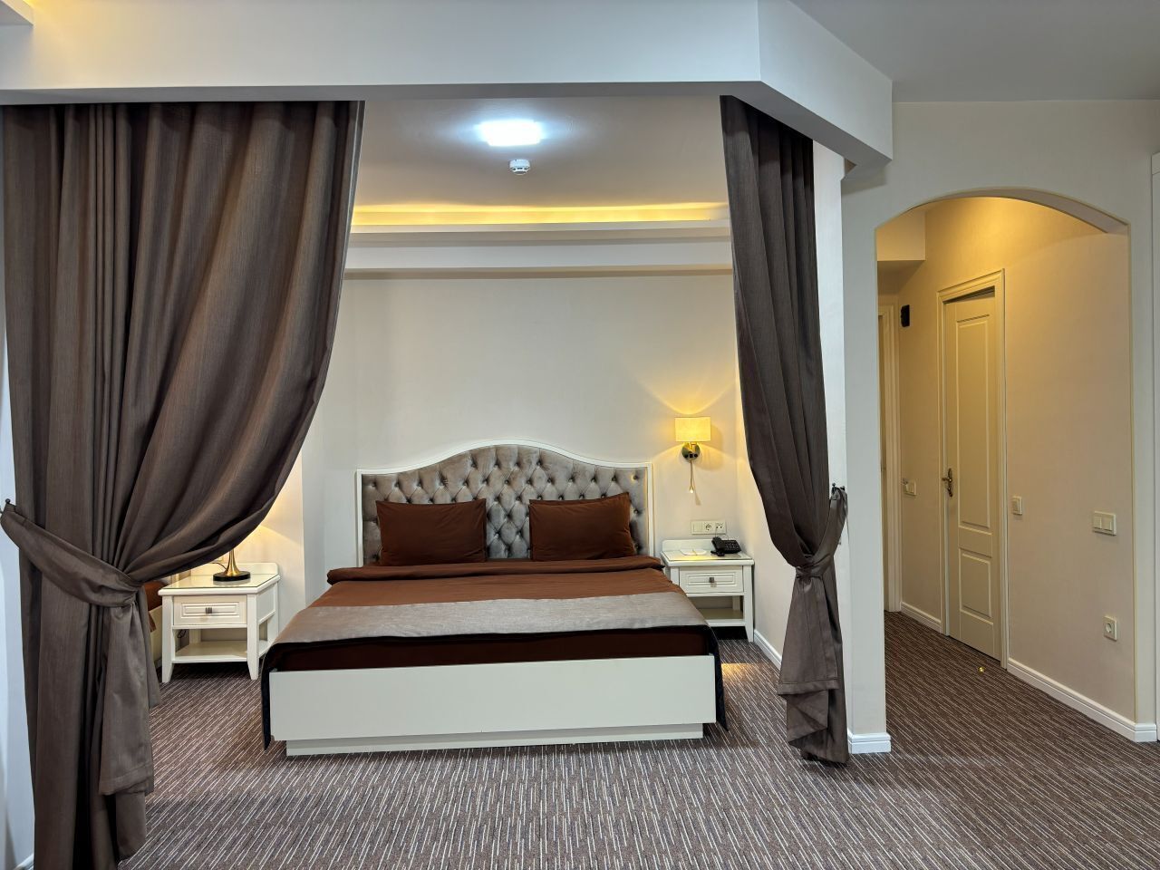 Une chambre à coucher avec un grand lit, deux tables de chevet, une lampe et une porte.