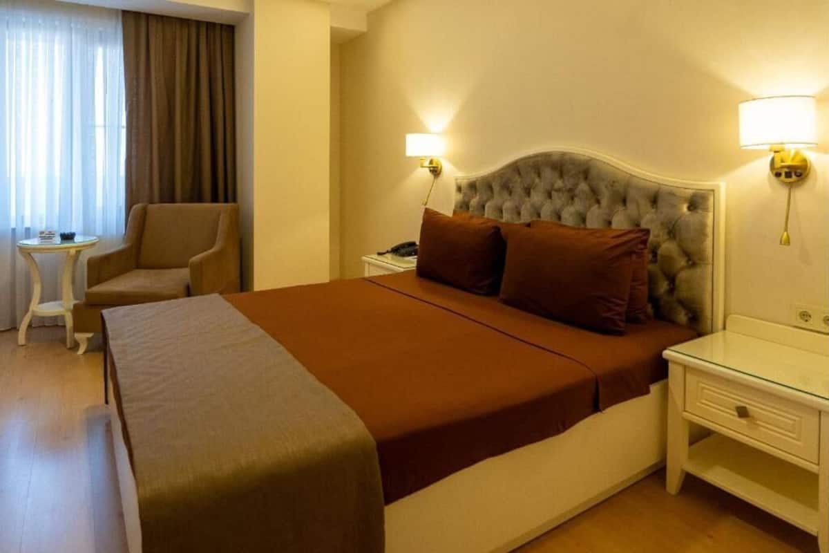 Quarto de hotel com cama, uma cadeira, uma mesinha e duas luminárias de cabeceira.