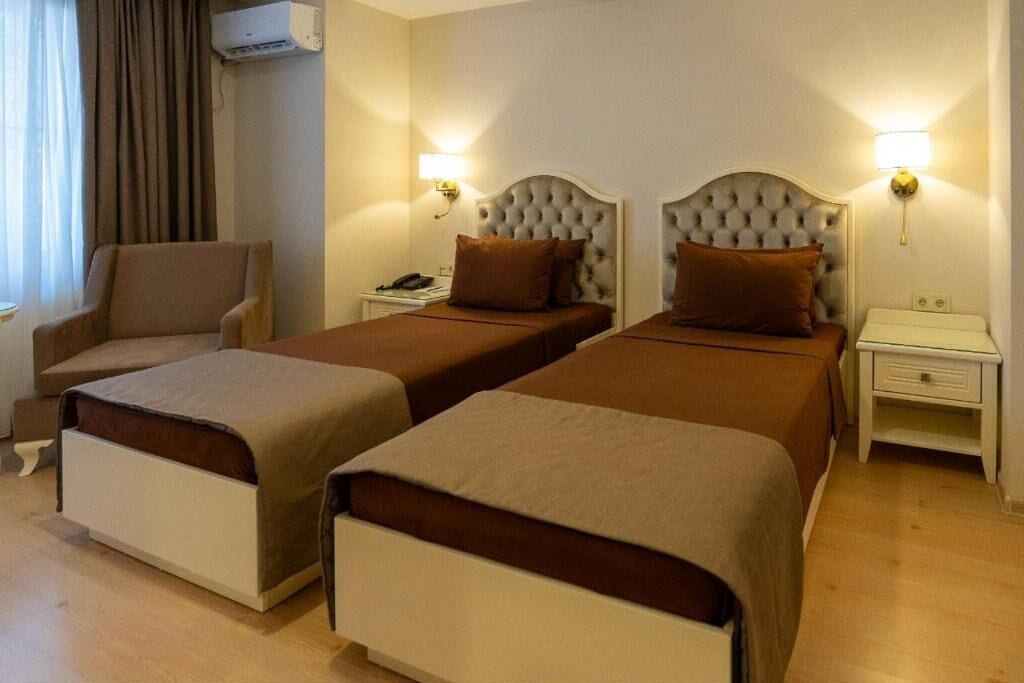 Habitació d'hotel amb dos llits individuals, una cadira, taules de nit amb làmpades i un aparell d'aire condicionat.