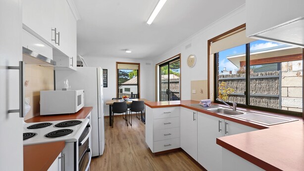 Une cuisine moderne équipée d’une cuisinière, d’un four à micro-ondes et d’un évier, un coin repas avec des chaises, et une grande fenêtre donnant sur l’extérieur.