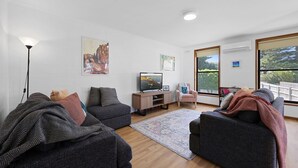 Un salon avec un canapé, un téléviseur, une petite table et une fenêtre donnant sur un beau paysage.