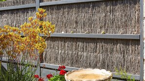 Une clôture en bois à la texture tissée, une mangeoire et un nichoir.
