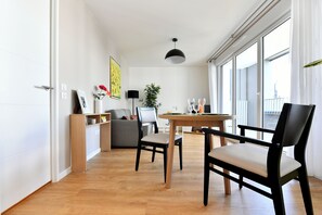 Una sala de estar moderna con un sofá, una mesa de comedor con sillas, una planta en maceta y un ventanal grande.