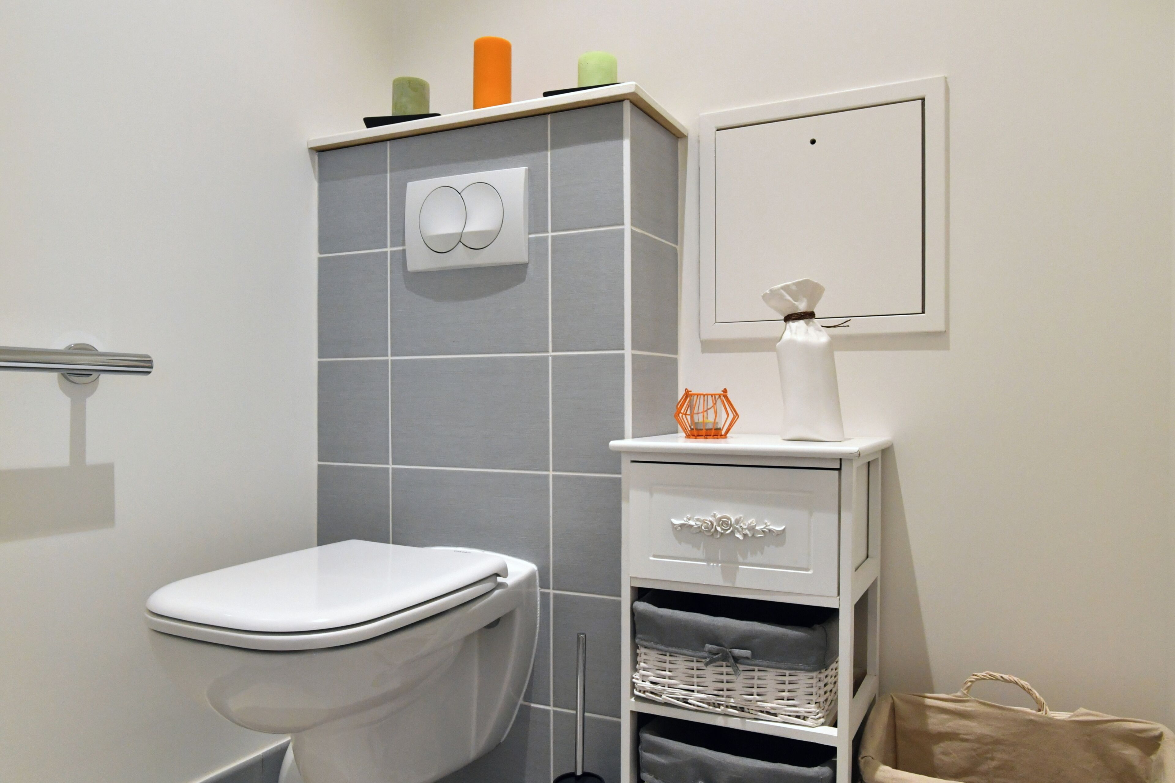 A bathroom with a toilet, a towel rack, a shelf with toiletries, and a framed picture on the wall.
