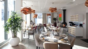 A modern dining area with tables set for meals, a large potted plant, and a kitchen area with cabinets. - Zenao Appart'hôtels Massy (Massy)