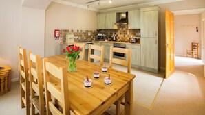 Eine moderne Küche mit Holzschränken, einer Mikrowelle und einem Toaster. Ein Esstisch mit Stühlen und eine Vase mit Blumen sind ebenfalls vorhanden.