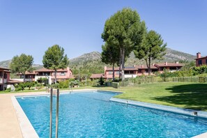 A swimming pool with a clear blue water, surrounded by buildings with red-tiled roofs, and a mountain in the background. - Apartment Gran Terraza Exclusive Costa Dorada (Bonmont Terres Noves)