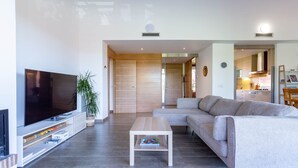 A modern living room with a flat-screen TV, a wooden coffee table, a grey sofa, and a kitchen area in the background. - Apartment Gran Terraza Exclusive Costa Dorada (Bonmont Terres Noves)