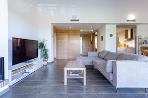 A modern living room with a flat-screen TV, a wooden coffee table, a grey sofa, and a kitchen area in the background. - Apartment Gran Terraza Exclusive Costa Dorada (Bonmont Terres Noves)