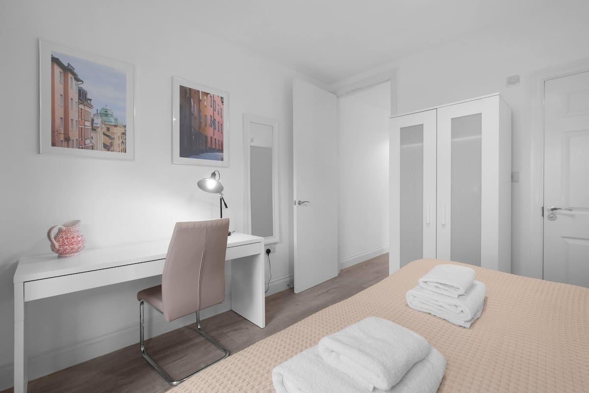 A hotel room with a bed, a desk, a chair, a lamp, and two doors.